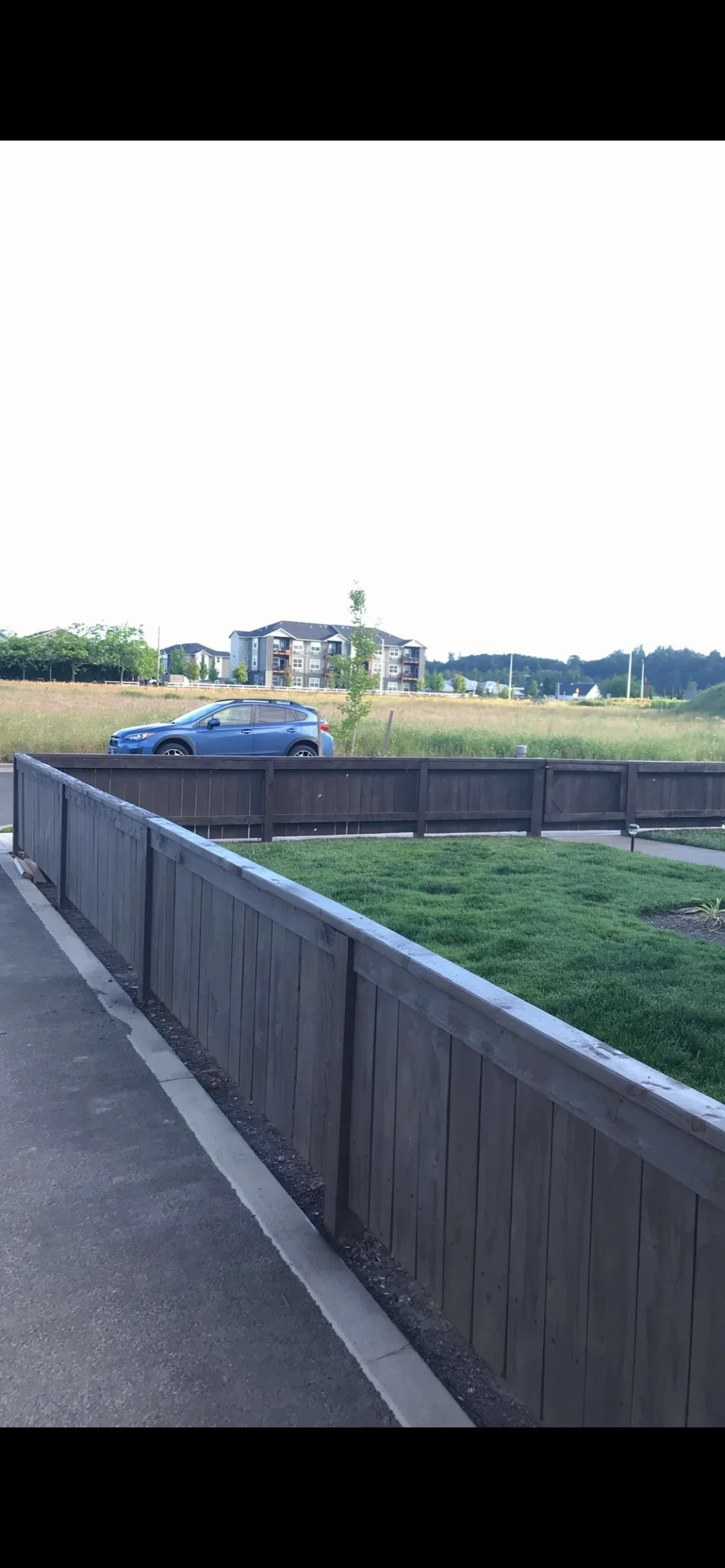 Dark composite privacy fence with concrete footer and landscape edging along residential property