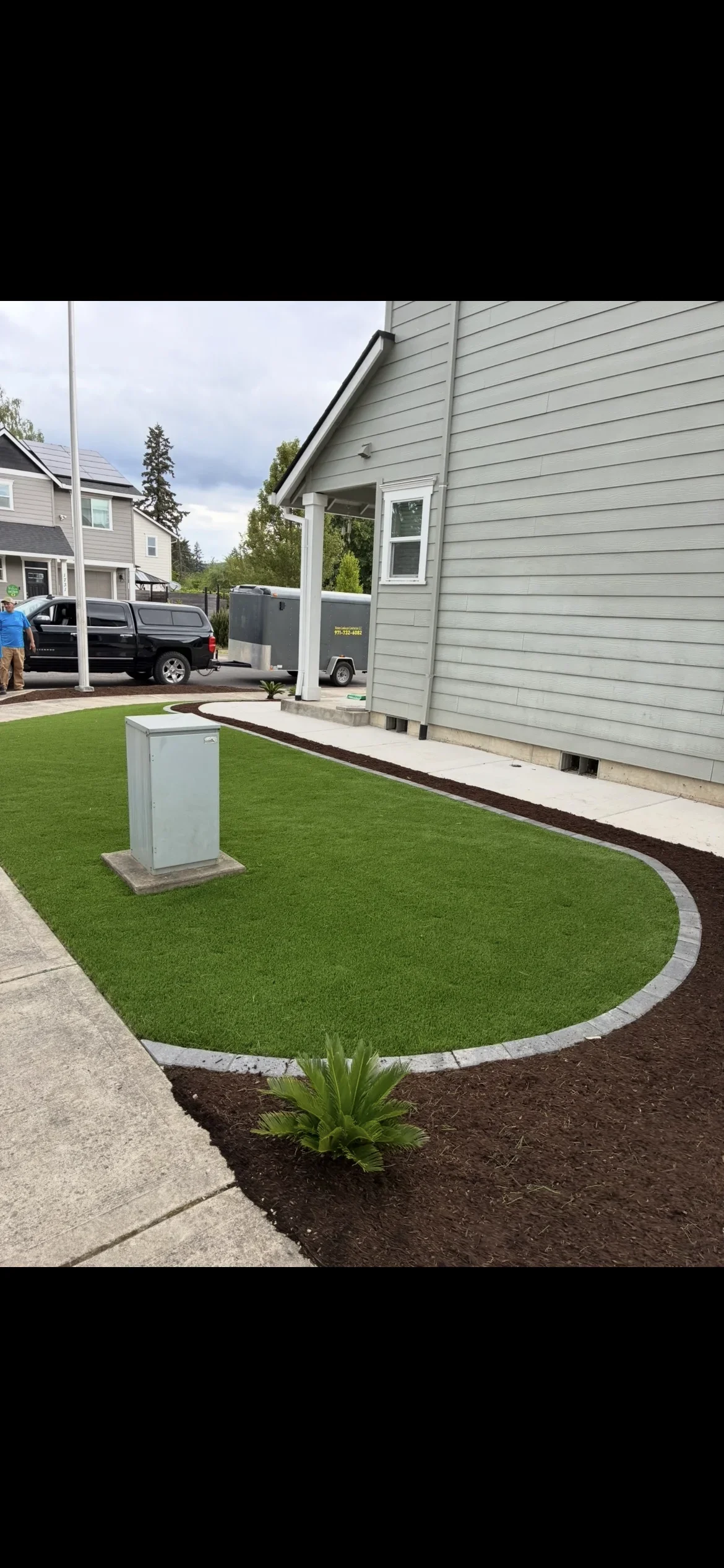 Artificial turf yard with concrete edging, dark mulch beds, and utility box near house