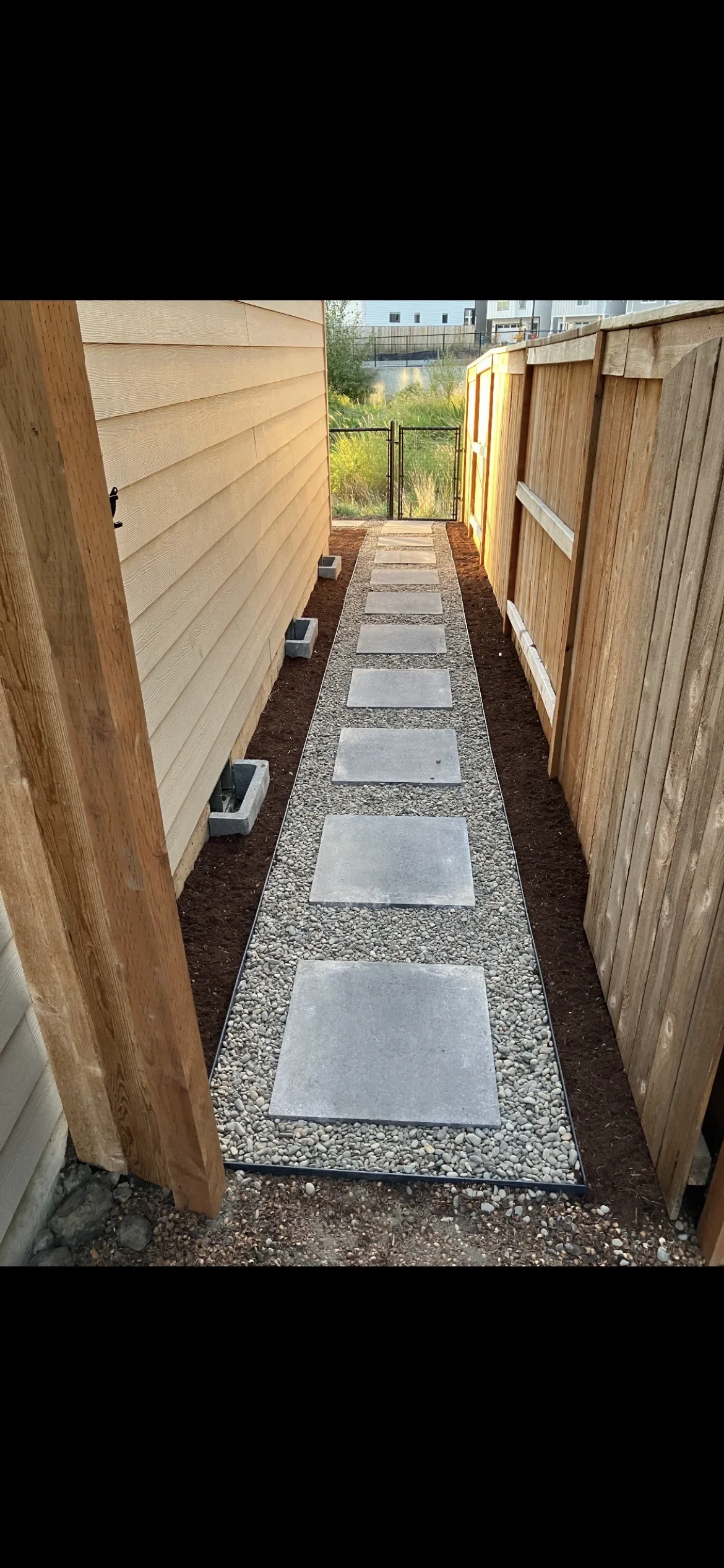 Concrete stepping stones with river rock border and mulch in narrow side yard between wood fences
