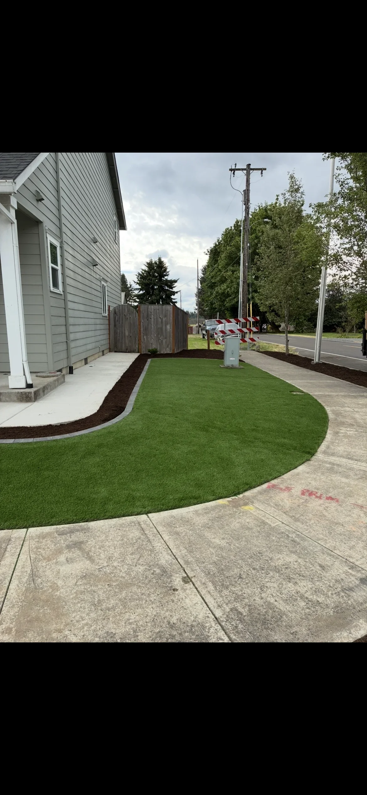 Synthetic turf lawn with curved edges, concrete patio, mulch beds, and residential home exterior
