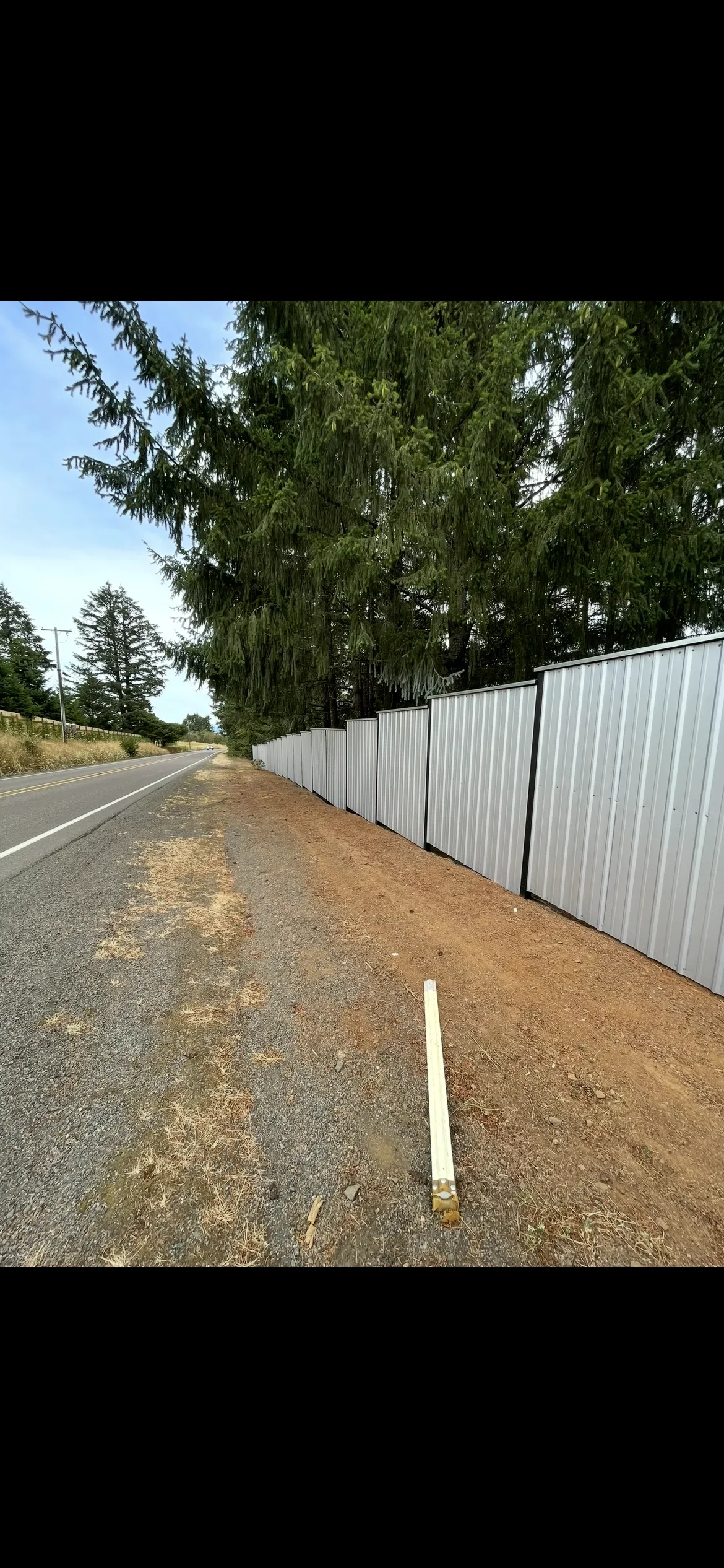 White corrugated metal fence with black posts installed along graded dirt roadside