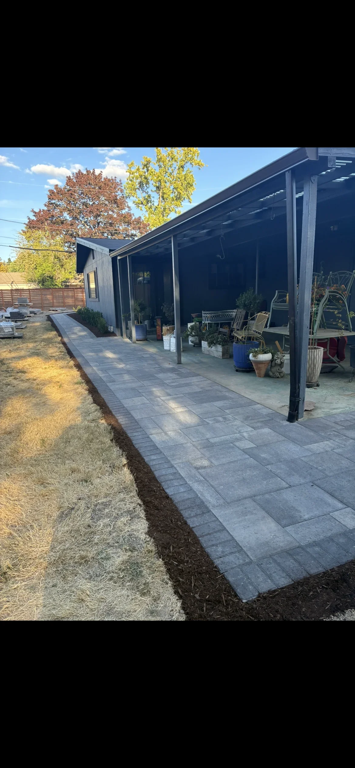 Gray paver patio with black steel pergola and shade panels, mulch edging